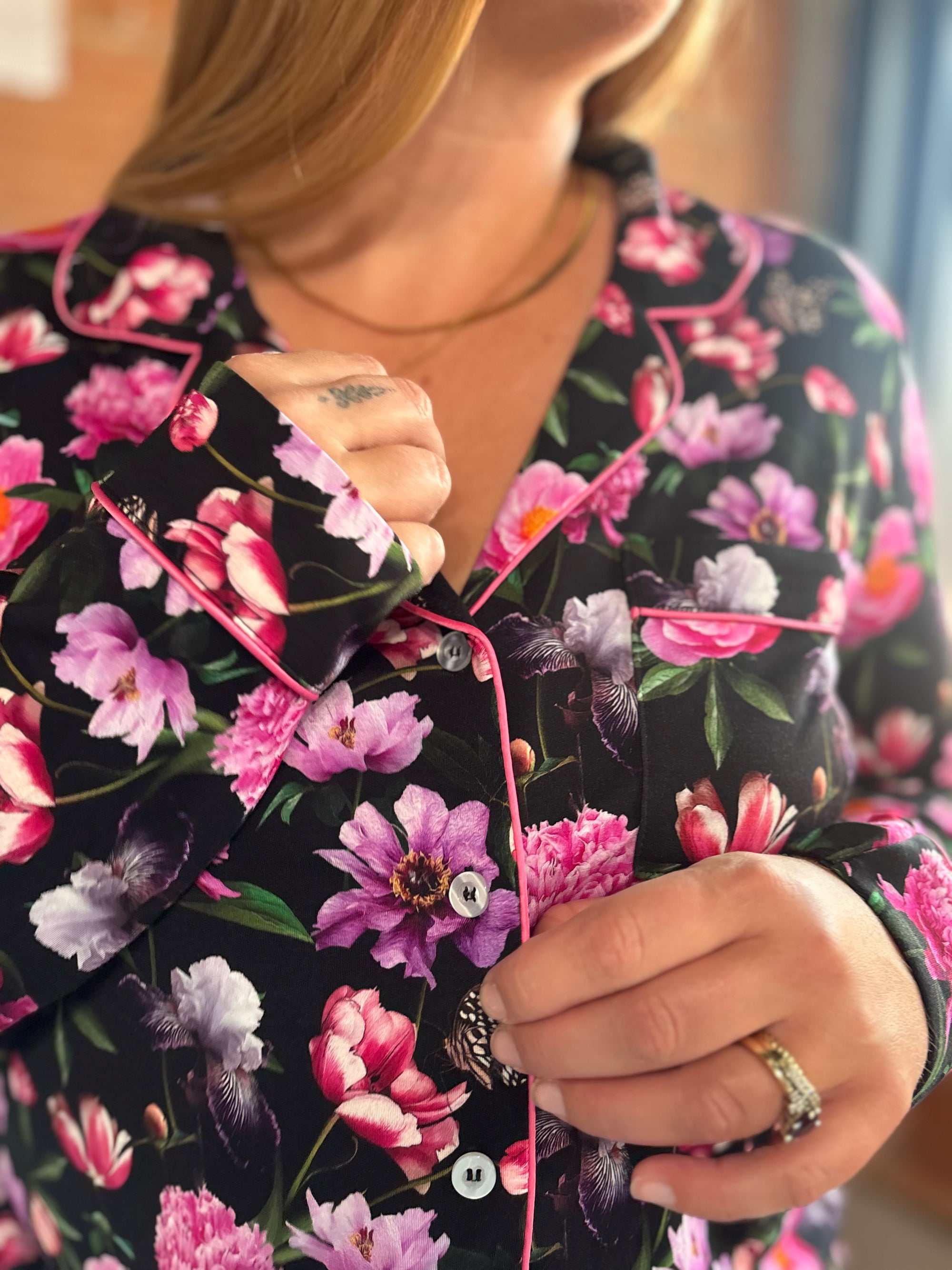 A close-up of a person wearing a black long-sleeve pajama top with a vibrant pink, purple, and green floral print and pink piping trim.